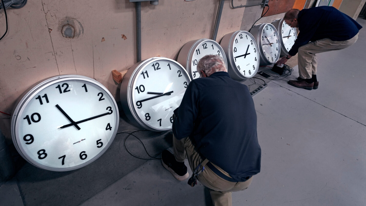 FILE - Clockmakers Rich Finn, left, and Tom Erb adjust the time zone controllers on a series of clo...